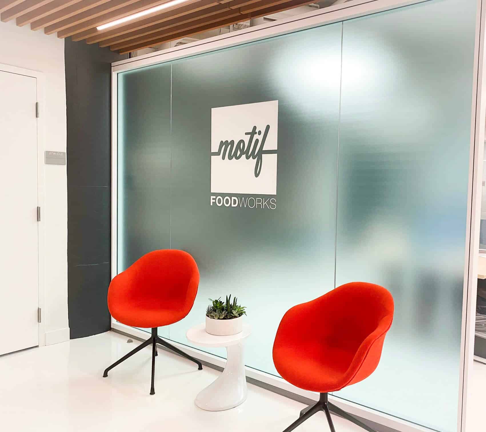 two-red-chairs-sitting-in-front-of-blurred-out-glass-window-with-"motif"-logo.