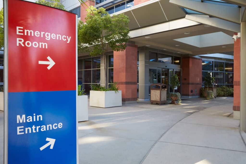 The outside of a hospital entryway featuring signage that directs visitors and incoming patients to the emergency room and main entrance.