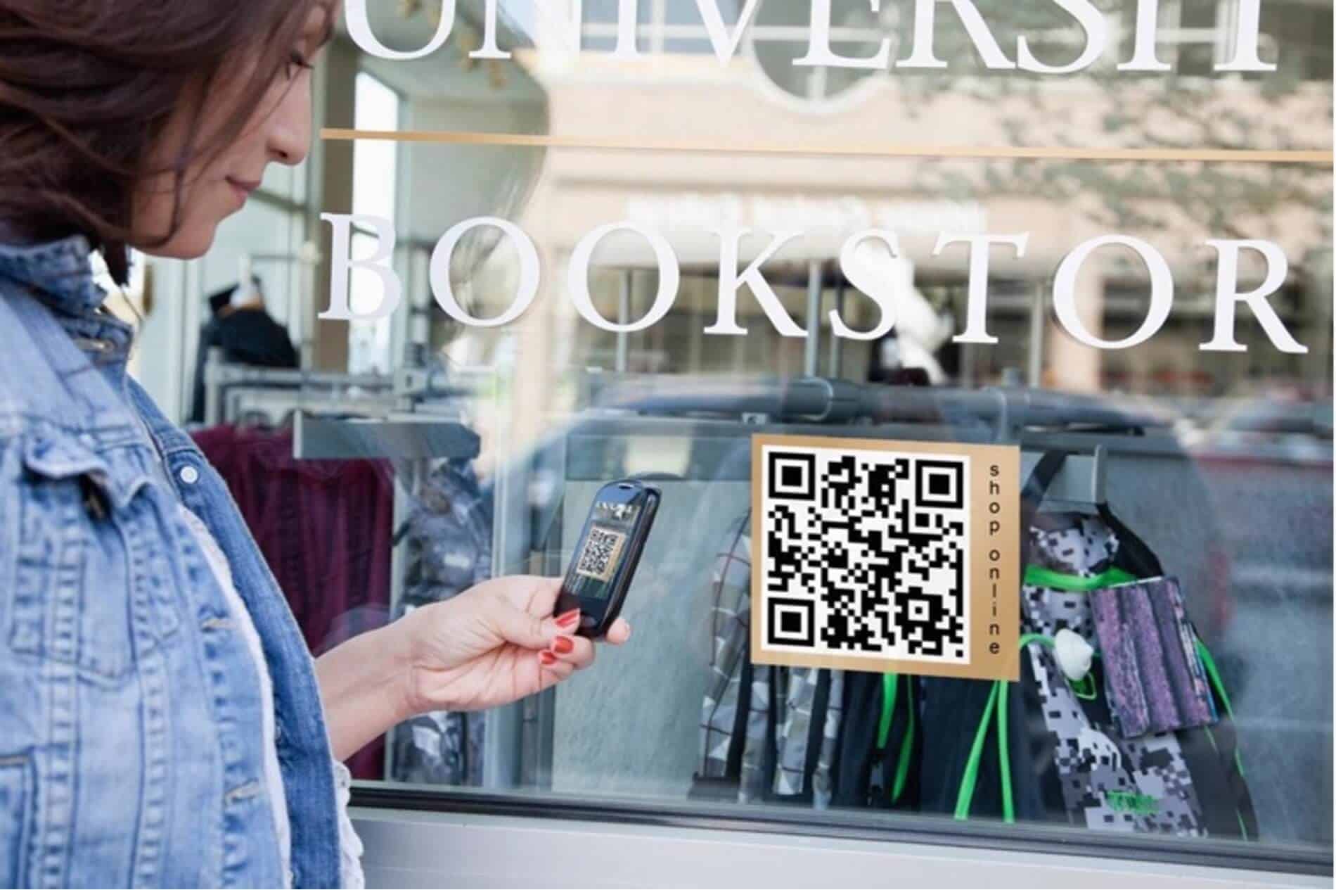 A QR code displayed on the outside of a bookshop window. A woman in a denim jacket scans the code using her smartphone.