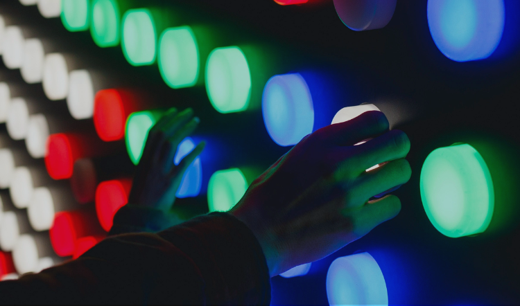 Hand touching large-format LED pixels on a video wall panel showing red, green, and blue light clusters up close