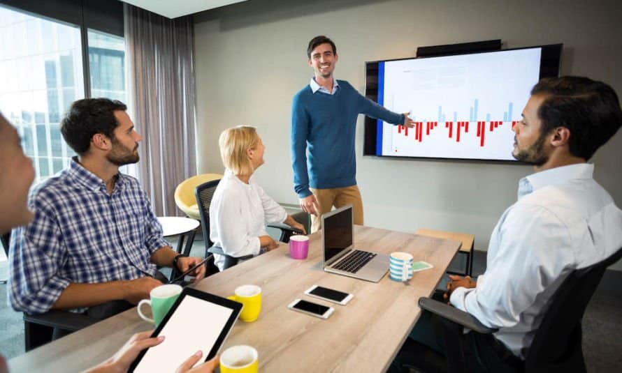 Man presenting on a tv in front of other team members