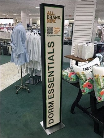 A vertical sign advertising dorm essentials set up in a department store. It features a QR code that customers can use to receive a shopping check list.