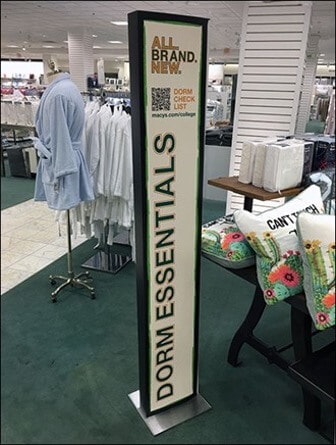 A vertical sign advertising dorm essentials set up in a department store. It features a QR code that customers can use to receive a shopping check list.