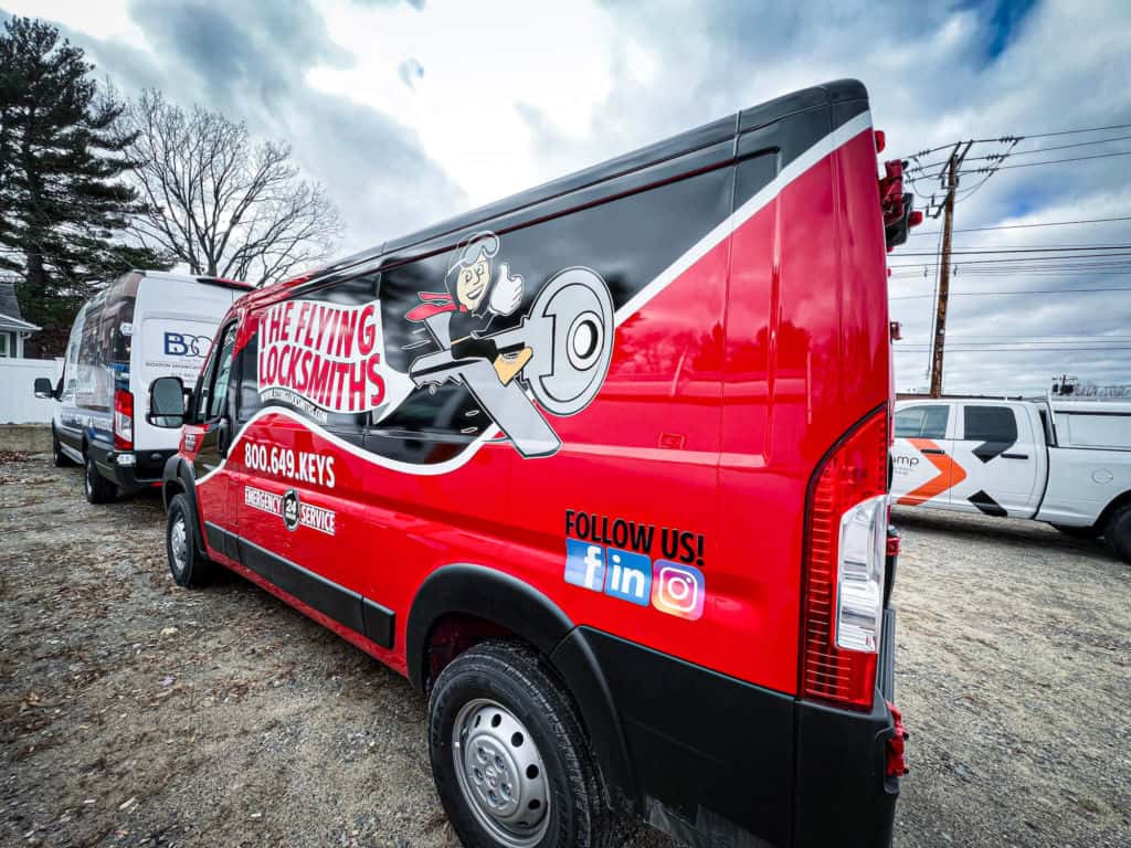 A black and red vehicle wrap featuring a locksmith company name, logo and contact information appears on a cargo van.