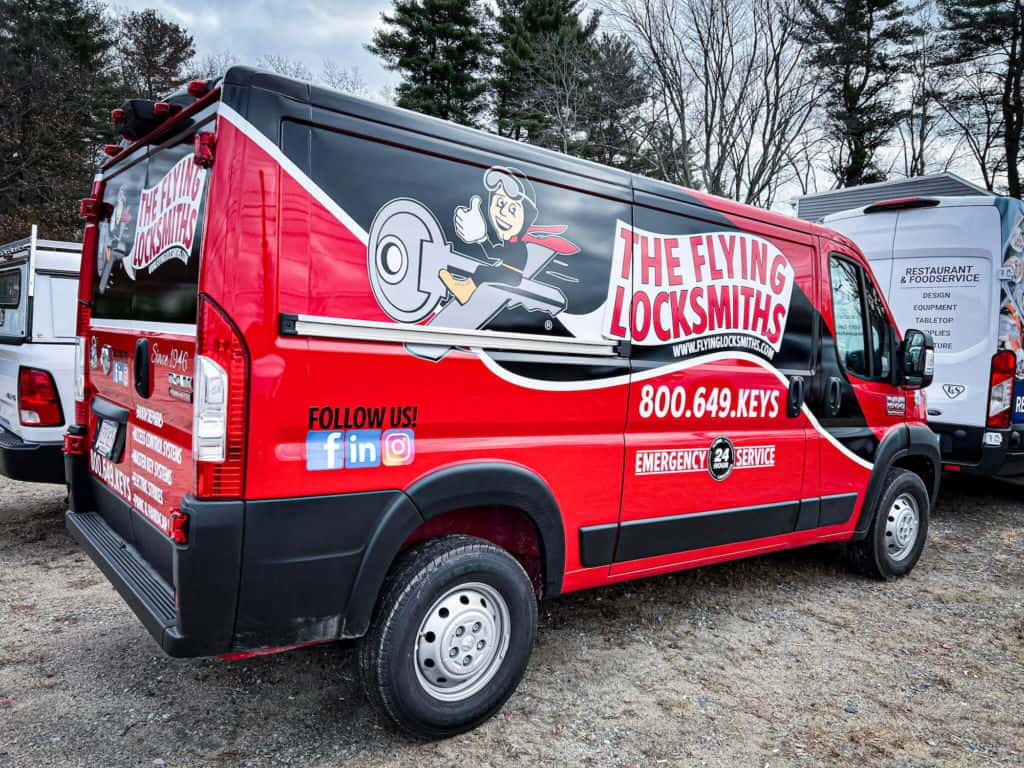 A cargo van for a locksmith company features a black and red vehicle wrap with the name, contact information and social media pages of the business.