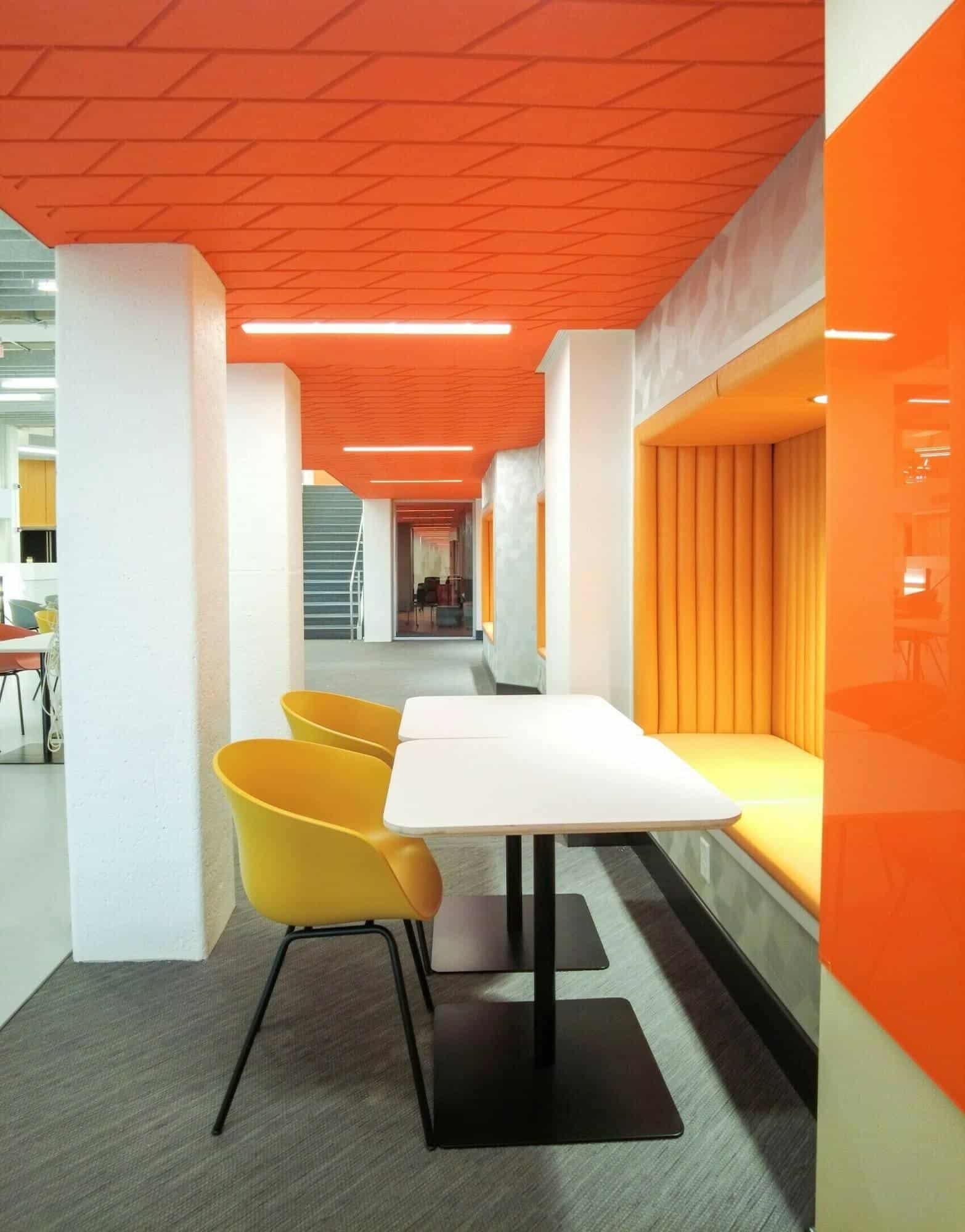 side-view-of-two-yellow-chairs-at-a-white-table.work-table-is-an-orange-colored-office-that-is-promoting-green--technologies.