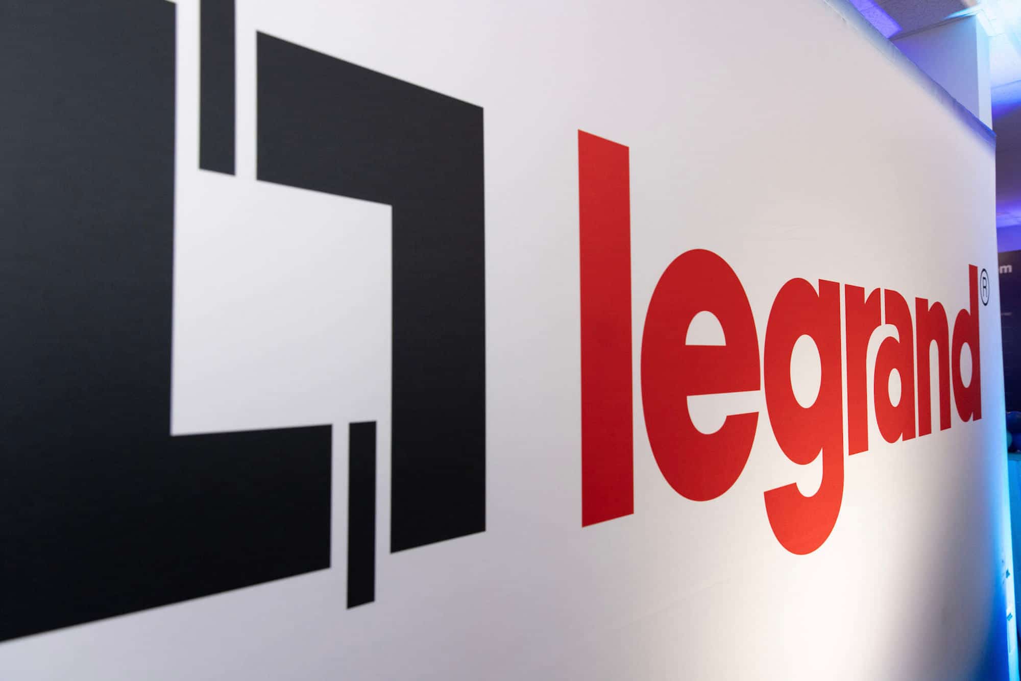 A white trade show booth backdrop featuring a company logo and red writing that reads "legrand."