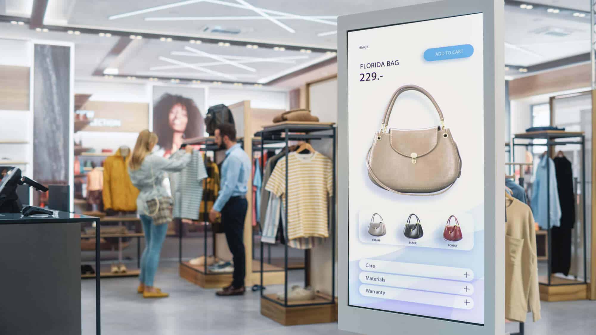 A-digital-sign-illuminates-an-advertisement-for-a-purse-while-shoppers-browse-racks-of-clothing-nearby.