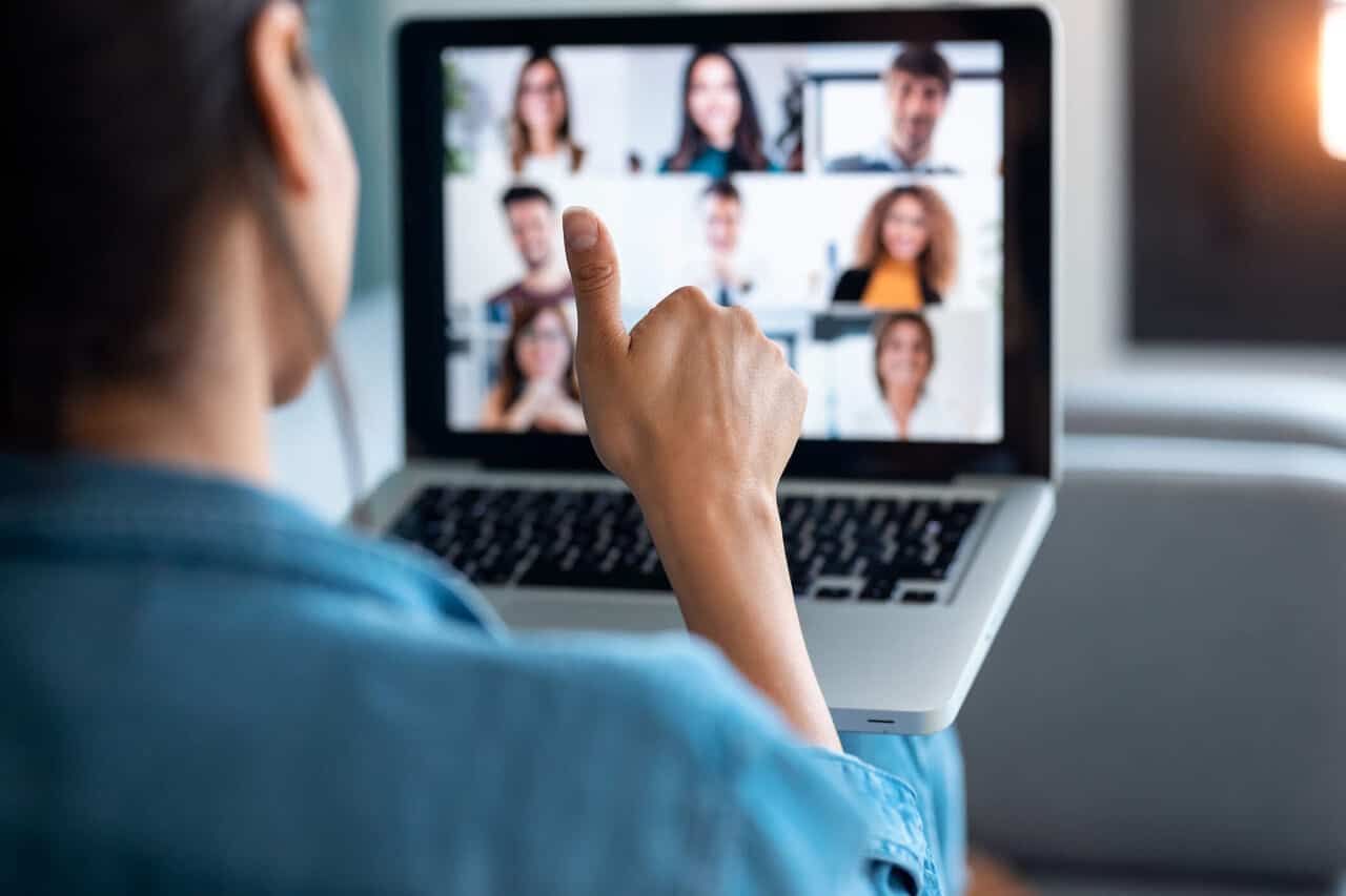 An image showing an employee from behind giving a thumbs up during a video call that they're attending on a laptop.